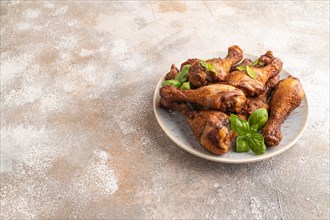 Smoked chicken legs with herbs and spices on a ceramic plate on a brown concrete background. Side