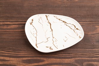 Empty white with golden pattern ceramic plate on brown wooden background. Side view, copy space