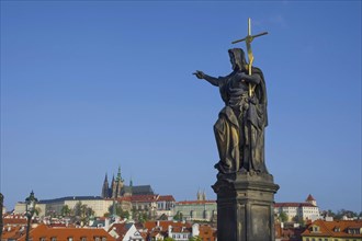 Statue of St. John the Baptist on Charles Bridge, with Hradcany castle and St. Vitus Cathedral in