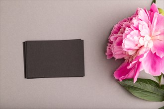 Black business card with pink peony flowers on gray pastel background. top view, flat lay, copy