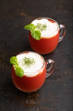 Tomato juice with basil and sour cream in glass on a black concrete background. Healthy drink