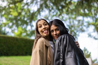 Two female friends together happily looking at the camera with tree branches behind them