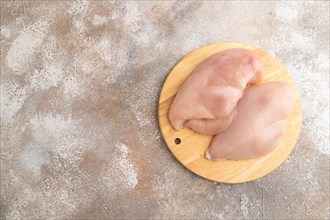 Raw chicken breast on a wooden cutting board on a brown concrete background. Top view, flat lay,