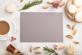 Gray paper sheet mockup with cup of coffee, almonds and macaroons on gray concrete background.