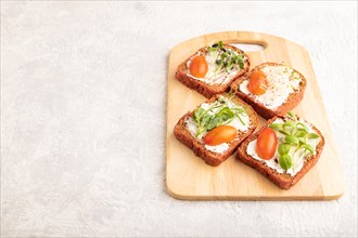 Red beet bread sandwiches with cream cheese, tomatoes and microgreen on gray concrete background.