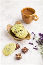 Green cookies with chocolate and mint on leaflike ceramic plate with cup of coffee on gray concrete