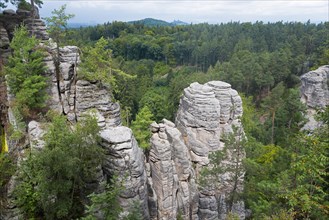 Majestic rock formations rise up in the middle of a dense forest under a cloudy sky, Prachovske