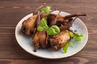 Smoked quails with herbs and spices on a ceramic plate on a brown wooden background. Side view,