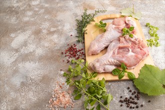 Raw turkey wing with herbs and spices on a wooden cutting board on a brown concrete background.