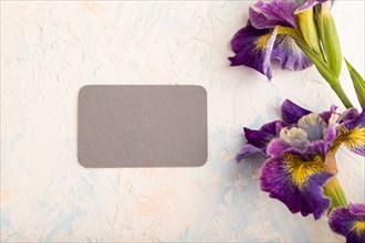 Gray business card with lilac iris flowers on white concrete background. top view, flat lay, copy