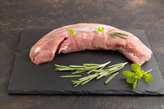 Raw pork meat with herbs and spices on slate cutting board on black concrete background. Side view,