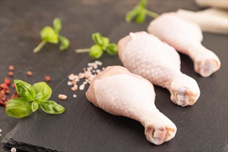 Raw chicken legs with herbs and spices on a black slate cutting board on a black concrete