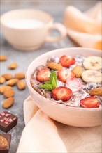 Chocolate cornflakes with milk, strawberry and almonds in ceramic bowl on gray concrete background