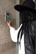 Vertical Side view of unrecognizable woman wearing a hat pushing the button of the intercom of