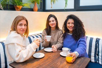 Three female friends looking at camera taking coffee together in a cute cafeteria