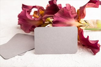 Gray business card with iris burgundy purple flowers on white concrete background. side view, copy