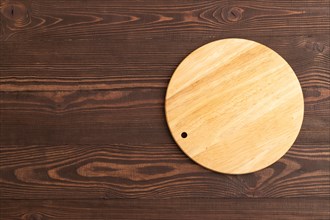 Empty round wooden cutting board on brown wooden background. Top view, copy space, flat lay