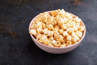 Popcorn with caramel in ceramic bowl on a black concrete background. Side view, close up