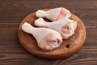 Raw chicken legs on a wooden cutting board on a brown wooden background. Side view, close up