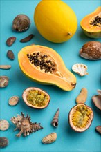 Ripe cut papaya, melon, passion fruit, seashells, pebbles on blue pastel background. Side view,