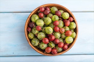 Fresh red and green gooseberry in wooden bowl on blue wooden background. top view, flat lay, close