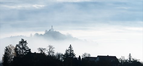 A misty landscape with silhouettes of trees and a chapel on a hill, Wurmlinger Kapelle