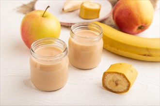 Baby puree with fruits mix, apple, banana infant formula in glass jar on white wooden background.