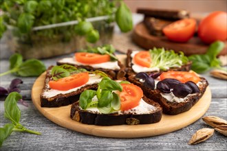 Grain rye bread sandwiches with cream cheese, tomatoes and basil microgreen on gray wooden