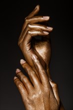 Beautiful man's hands in golden paint on black background close up