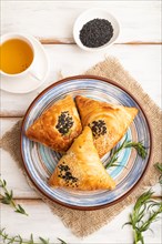 Homemade asian pastry samosa, cup of green tea on white wooden background and linen textile. top
