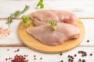 Raw chicken breast with herbs and spices on a wooden cutting board on a white wooden background.