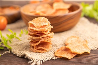 Slices of dehydrated salted meat chips with herbs and spices on brown wooden background and linen