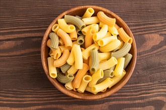 Rigatoni colored raw pasta with tomato, eggs, spices, herbs on brown wooden background. Top view,
