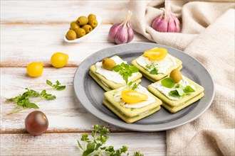 Green cracker sandwiches with cream cheese and cherry tomatoes on white wooden background and linen
