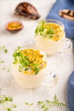 Yogurt with passionfruit and marigold microgreen in glass on gray concrete background with blue