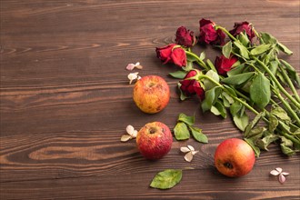 Withered, decaying, roses flowers and apples on brown wooden background. side view, copy space,
