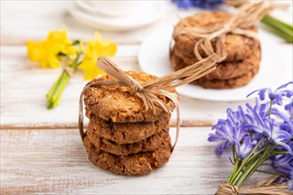 Oatmeal cookies with spring snowdrop flowers bluebells, narcissus and cup of coffee on white wooden