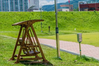 Wooden swing park bench beside walkway with city buildings in background in South Korea