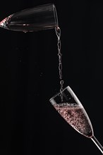 Rose champagne flows from one champagne glass into another, captured in motion, black background