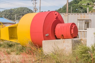 Top view of large yellow and red ocean buoy laying in grass in front of old rusty storage building