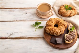 Homemade sweet bun with chocolate cream and cup of coffee on a white wooden background and linen