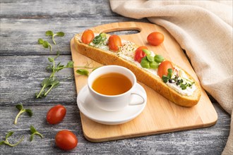 Long white bread sandwich with cream cheese, tomatoes and microgreen on gray wooden background and