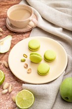Green macarons or macaroons cakes with cup of coffee on a brown concrete background and linen