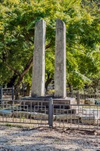 Ancient stone carved flag pole supports in front of lush green trees at Buddhist temple in