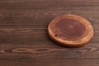 Empty round wooden cutting board on brown wooden background. Side view, copy space