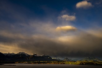 Lake Hopfensee with stormy sky in soft morning light and Allgaeu mountains in the background,