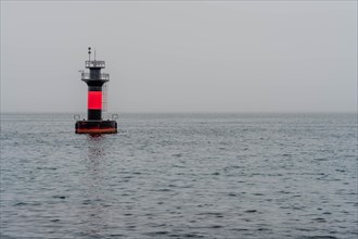 Red and black lighthouse in waters offshore on overcast morning in Jeju, South Korea, Asia