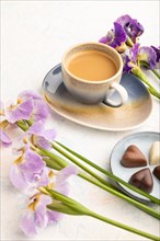 Cup of cioffee with chocolate candies and lilac iris flowers on white concrete background. side