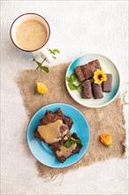 Chocolate brownie with caramel sauce with a cup of coffee on gray concrete background and linen