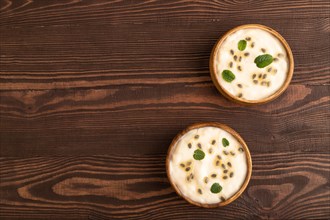Yoghurt with granadilla and mint in wooden bowl on brown wooden background. top view, flat lay,